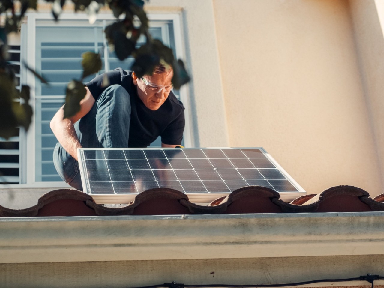 Man in a black shirt installing a solar panel on a roof. 